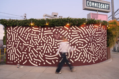 Person walking past a decorative wall with a pattern and 'Commissary' sign in the background.